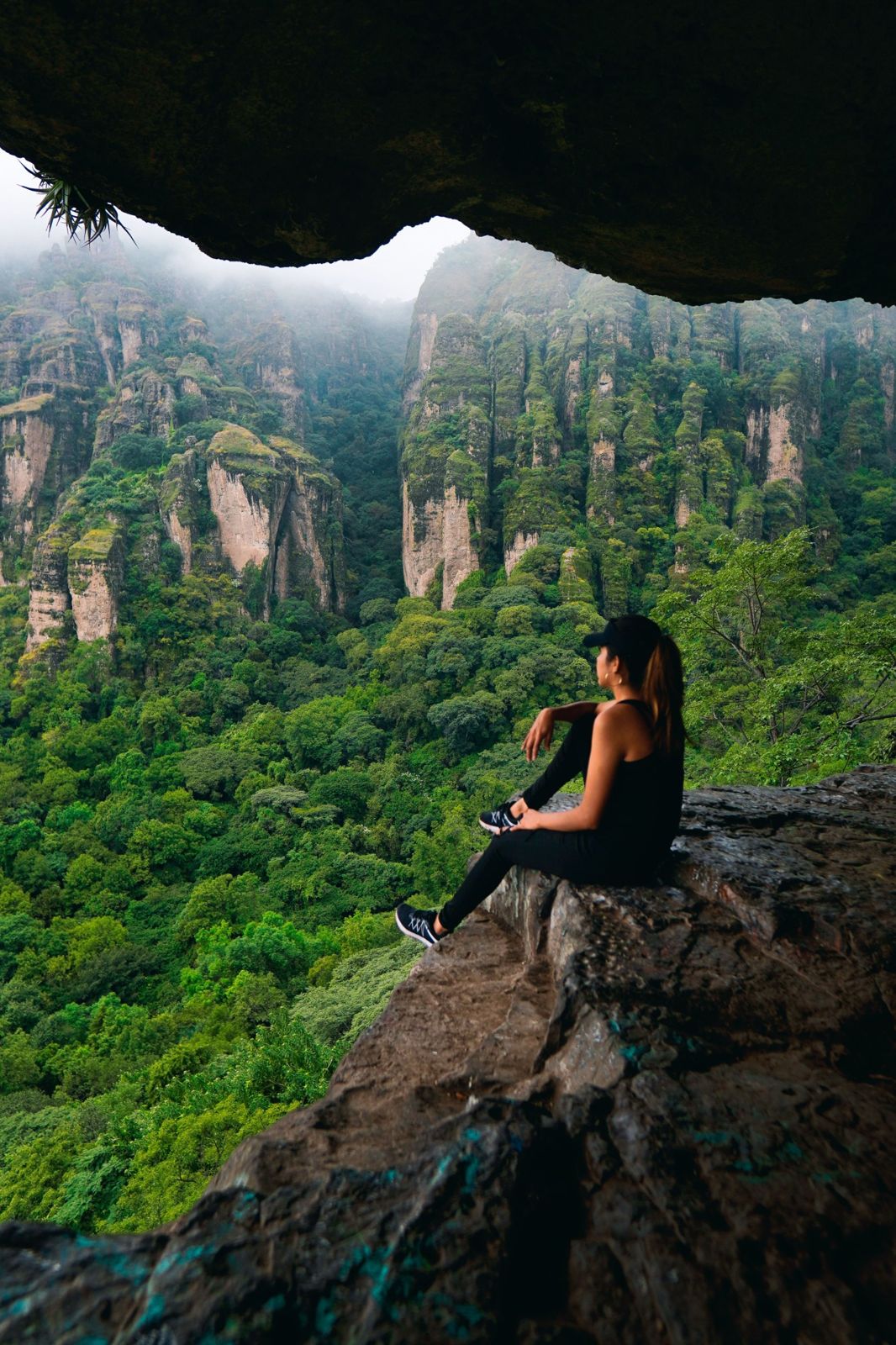 Persona sentada bajo una roca mirando los riscos de Tepoztlán entre la niebla